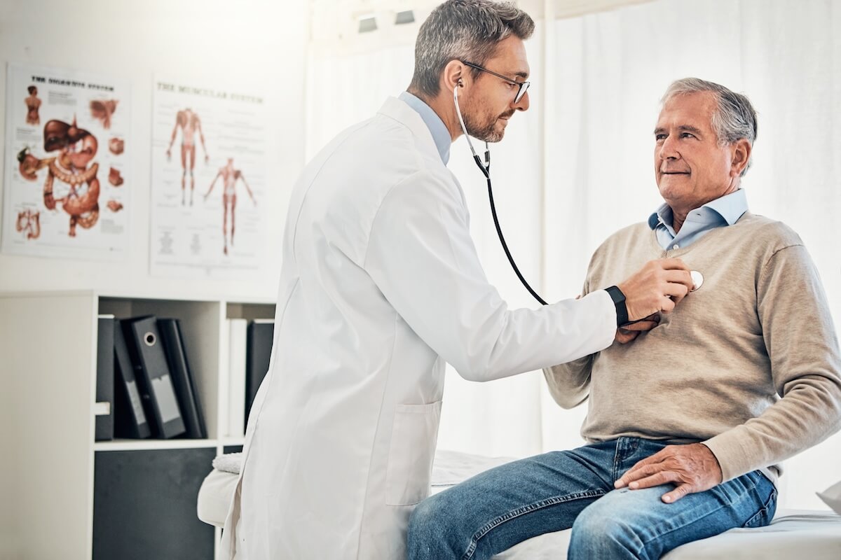 common heart conditions Consultation, man and doctor in office with stethoscope, checkup and healthcare at senior clinic. Diagnosis, elderly patient and medical professional with support, checking heart health and advice